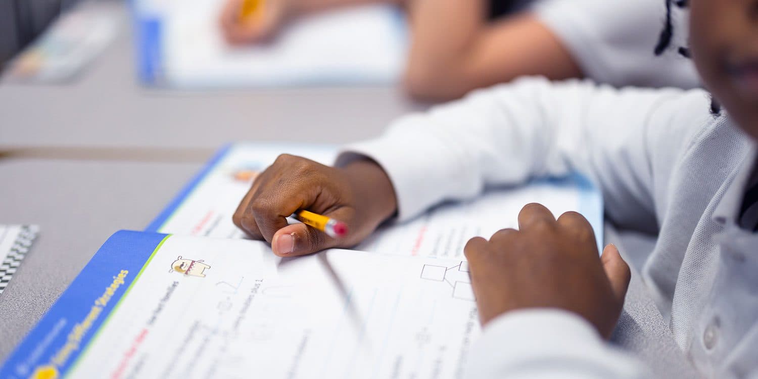 Student holding a pencil over an open math workbook.