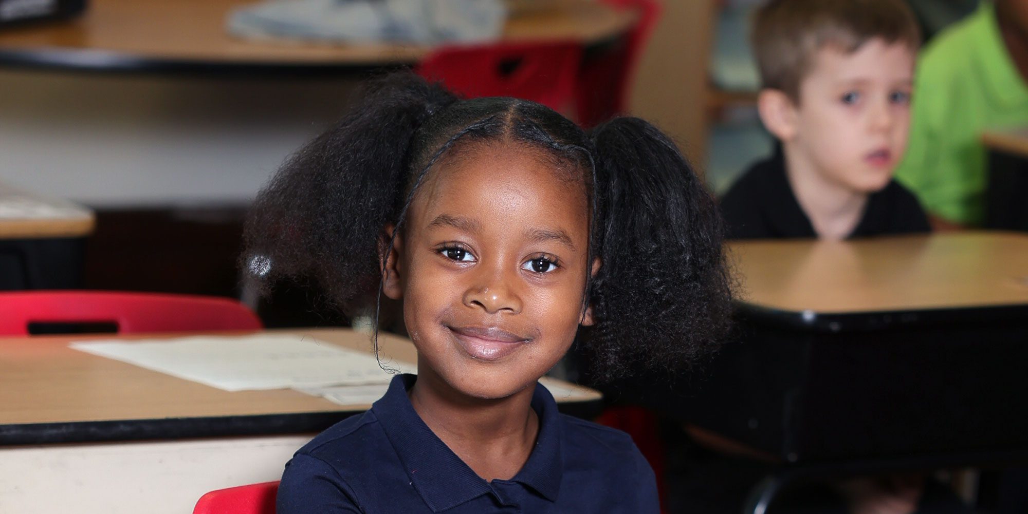 Smiling young student with pigtails at a classroom desk.